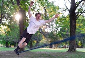 giovane uomo equilibratura e salto su slackline. uomo a passeggio, salto e equilibratura su corda nel parco. foto