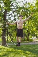 giovane uomo equilibratura e salto su slackline. uomo a passeggio, salto e equilibratura su corda nel parco. foto