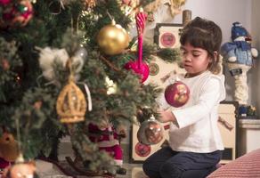 asiatico poco ragazza decorare il Natale albero al chiuso. il mattina prima natale. ritratto amorevole ragazza vicino su. foto