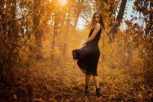 bellissimo giovane ragazza nel nero vestito in posa su telecamera nel d'oro autunno legna foto