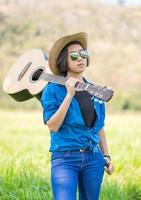 donna indossare cappello e trasportare sua chitarra nel erba campo foto