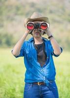 donna indossare cappello e hold binoculare nel erba campo foto