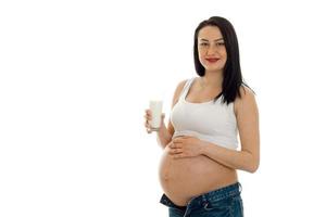 giovane allegro incinta madre isolato su bianca sfondo nel studio in posa con bicchiere di latte foto
