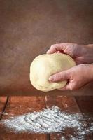 il mani di un anziano, paffuto donna siamo impasto Impasto su un' di legno tavolo. preparazione di Impasto per un' festivo torta, Pizza foto