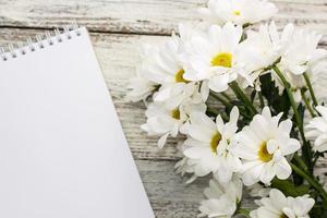 primavera mazzo di bianca margherite con pulito taccuino per Scrivi su bianca di legno tavolo foto