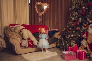 poco bambino ragazza con ballon nel sua mano guardare lontano con Natale albero dietro a sua foto