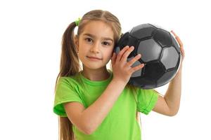 bellissimo poco ragazza con grigio calcio palla nel sua mani sembra a il telecamera foto