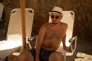 giovane uomo indossare un' cappello e bicchieri si abbronza a il spiaggia foto