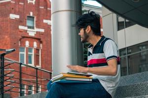 giovane alunno si siede su un' strada con libri e sembra verso foto