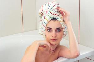 bellissimo giovane ragazza con asciugamano su il capelli bugie nel il bagno e sembra dritto foto