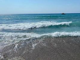 onde di acqua nel il mare e sabbia con piccolo naturale multicolore pietre su il riva del mare, piccolo ciottoli su il spiaggia. sfondo, struttura foto