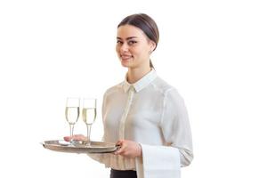 affascinante cameriera nel un' bianca camicia sorridente e Tenere Due bicchieri di vino su un' vassoio quello foto