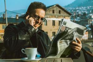 divertente adulto maschio leggere giornale parlando Telefono e potabile caffè foto