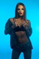 verticale ritratto di giovane bellissimo ragazza con rosso labbra nel jeans Abiti in posa su telecamera su blu sfondo foto