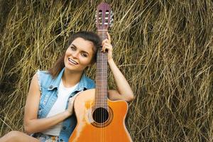 giovane e contento donna giocando chitarra nel il villaggio foto