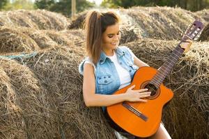 giovane e contento donna giocando chitarra nel il villaggio foto