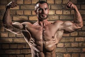 bodybuilder mostrando il suo muscoli contro mattone parete foto