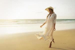 donna indossare bellissimo bianca vestito è a piedi su il spiaggia durante tramonto foto