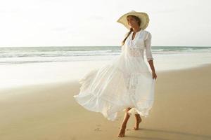 donna indossare bellissimo bianca vestito è a piedi su il spiaggia durante tramonto foto