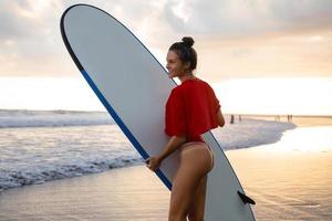 giovane e sexy donna con un' longboard durante fare surf sessione su il spiaggia foto