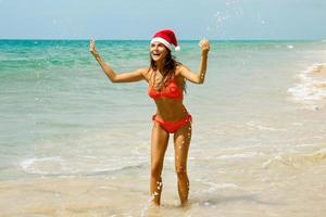 donna indossare bikini e Natale cappello su il spiaggia. inverno vacanze nel il caldo Paesi. foto