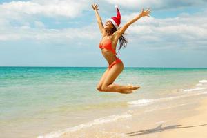 donna indossare bikini e Natale cappello su il spiaggia. inverno vacanze nel il caldo Paesi. foto