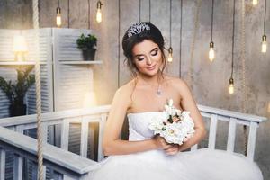 giovane contento sposa indossare bellissimo lussureggiante vestito nel il camera con un' lotto di leggero bulbi foto