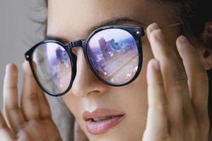 vicino su ritratto di giovane donna con un' riflessione di moderno città dentro occhiali foto
