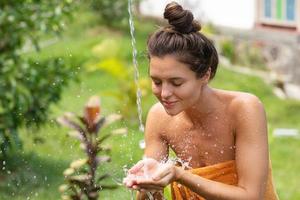 giovane donna lavaggio sua viso sotto all'aperto doccia foto