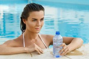 donna nel il nuoto piscina con un' bottiglia di acqua foto