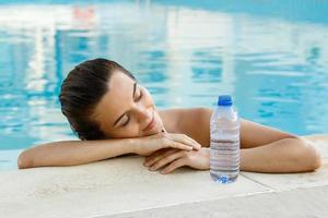 donna nel il nuoto piscina con un' bottiglia di acqua foto