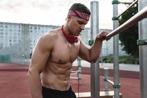 muscolare uomo indossare rosso bandana durante il suo ginnastica ritmica allenarsi su il strada foto