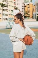 giovane elegante donna è in posa su il choi sospeso tenuta pallacanestro Tribunale foto