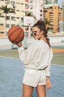 giovane elegante donna è in posa su il choi sospeso tenuta pallacanestro Tribunale foto