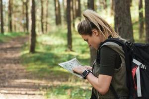 femmina escursionista con grande zaino utilizzando carta geografica per orientamento nel il foresta foto