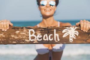 contento indossare costume da bagno con vecchio di legno cartello su il spiaggia foto