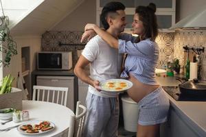 marito e il suo incinta moglie su il cucina durante prima colazione volta. foto