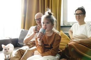 poco ragazza con un' karaoke microfono cantando per sua genitori foto