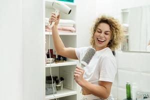 giovane contento donna utilizzando asciugacapelli dopo per sua Riccio capelli foto