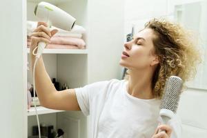 giovane contento donna utilizzando asciugacapelli dopo per sua Riccio capelli foto