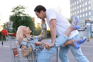 giovane coppia avere divertimento con un' shopping carrello su un' supermercato parcheggio foto