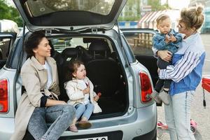 contento donne e loro bellissimo bambini accanto un' auto su un' parcheggio lotto foto