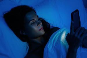 giovane donna è utilizzando smartphone a notte tempo nel il letto foto