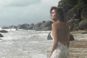 giovane donna indossare bellissimo bianca vestito è in posa su il spiaggia foto