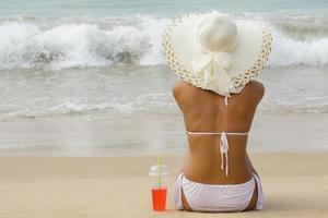 donna indossare a tesa larga cappello è seduta su il spiaggia foto