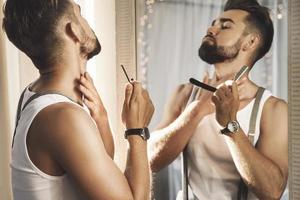 uomo guardare nel il specchio e rasatura il suo barba con un' dritto rasoio foto