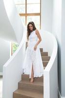 bellissima donna indossare bellissimo bianca vestito su un' scala dentro sua Casa foto