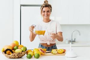 donna scrosciante appena spremuto fatti in casa arancia succo in il bicchiere nel moderno bianca cucina foto