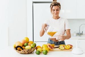 donna scrosciante appena spremuto fatti in casa arancia succo in il bicchiere nel moderno bianca cucina foto