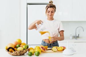 donna scrosciante appena spremuto fatti in casa arancia succo in il bicchiere nel moderno bianca cucina foto